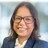 Portrait of Monica Pontes, Communications Manager, smiling in blue suit against blurry blue / grey office background.