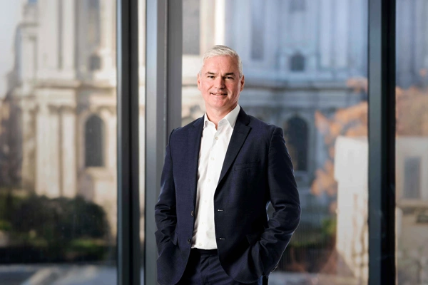 Vincent Clancy standing in the London office with the London city view in the background