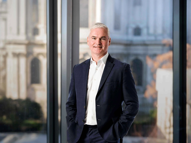 Vincent Clancy standing in the London office with the London city view in the background