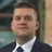 Dan Proud, Director, Infrastructure, UK, outside in front of a blurred brown background featuring a building and mix of natural and urban elements.