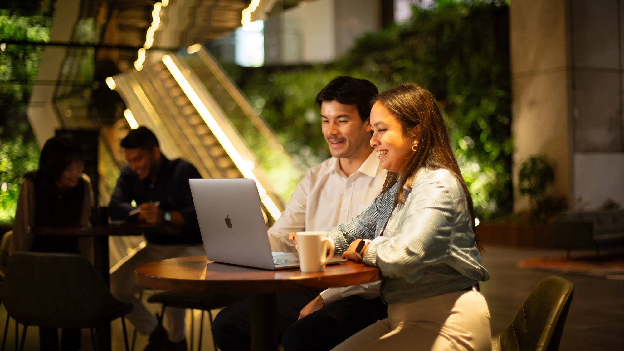 Two colleagues sitting together looking at a laptop in a plant-filled office.