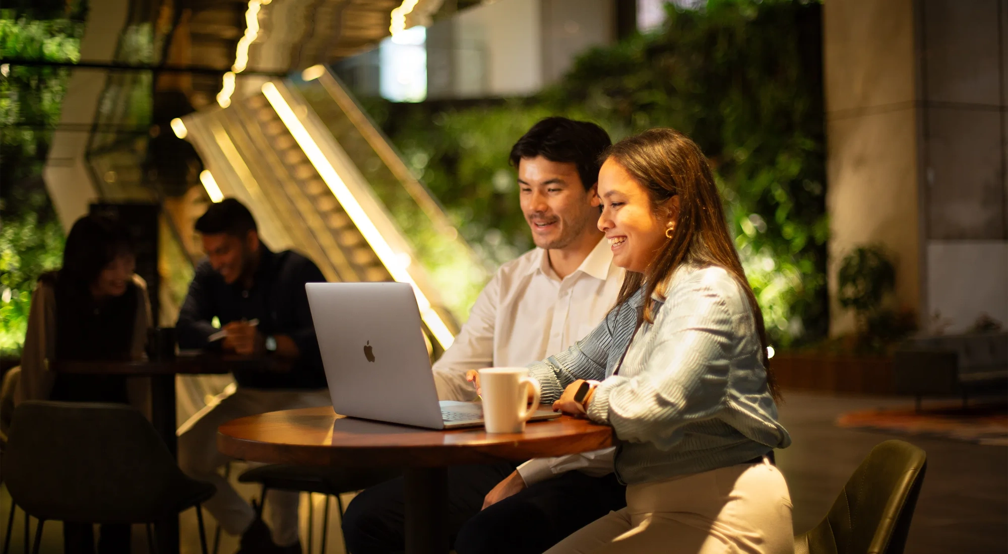 Two colleagues sitting together looking at a laptop in a plant-filled office.