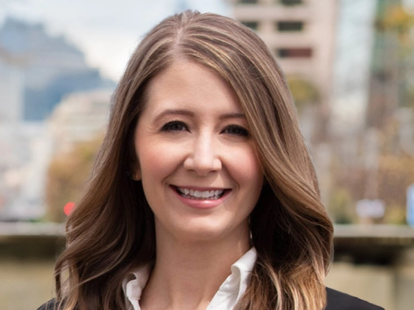 Whitney Knuf Ahn, Vice President, Nashville Cost Centre Leader, standing outside featuring an urban cityscape with tall buildings and a mix of architectural styles. The scene includes some trees with autumn foliage, adding a touch of color. 