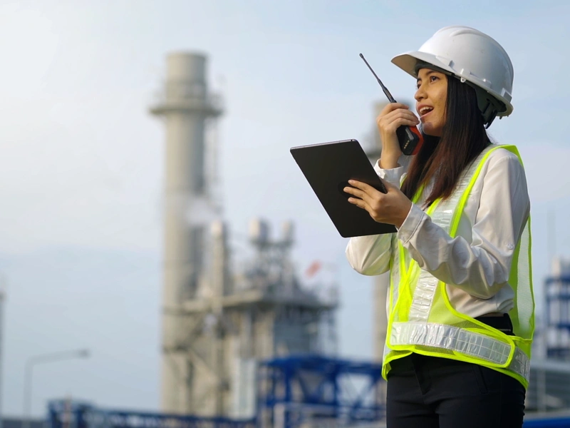 Woman with hard hat in high vis vest talking on a walkie talking at a plant