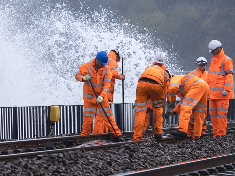 Workers wearing orange high vis working on a train track with water splashing