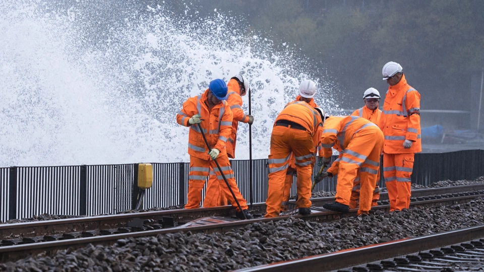 Workers wearing orange high vis working on a train track with water splashing
