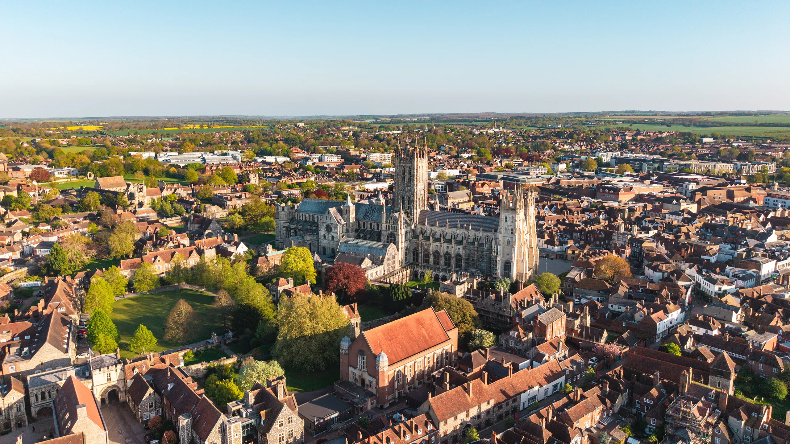 Canterbury Cathedral and historic city buildings from an aerial drone perspective, showing rooftops and trees