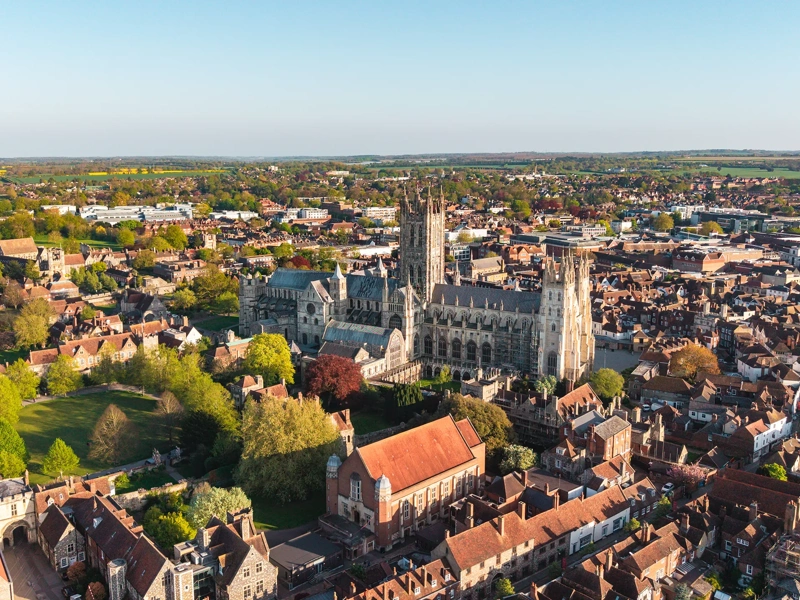 Canterbury Cathedral and historic city buildings from an aerial drone perspective, showing rooftops and trees