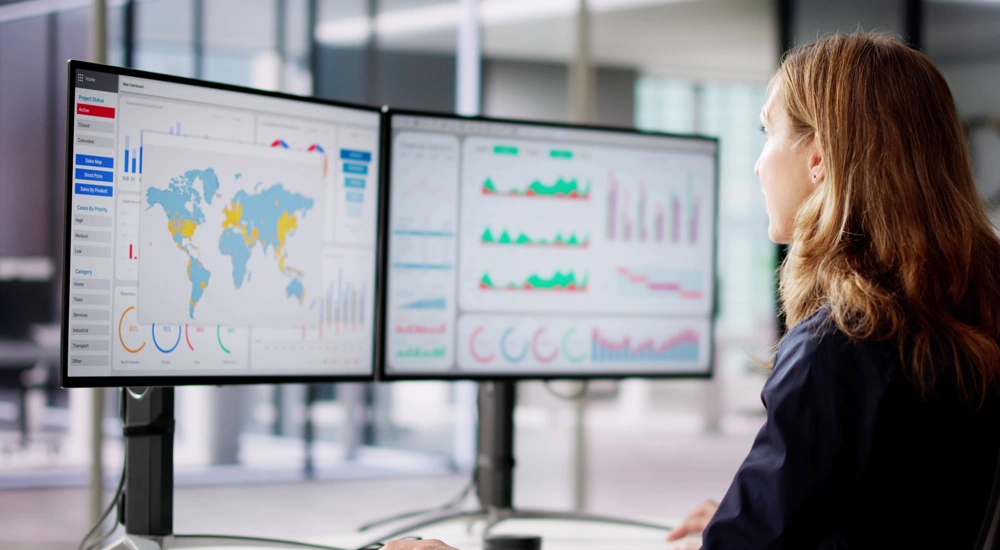 Woman looking at two screens displaying graphs