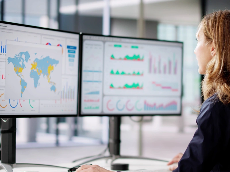 Woman looking at two screens displaying graphs