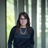 Liz Melendez standing outdoors in front of dense green foliage and landscaped bushes, with background softly blurred.