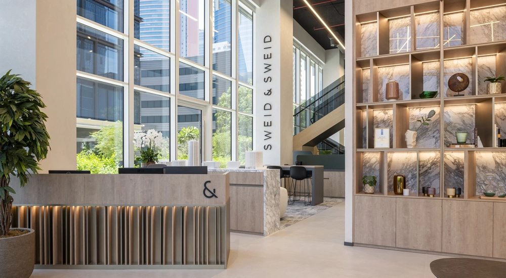 Interior of a warm, light-filled modern office with a shelf of objects and an orchid on the reception desk