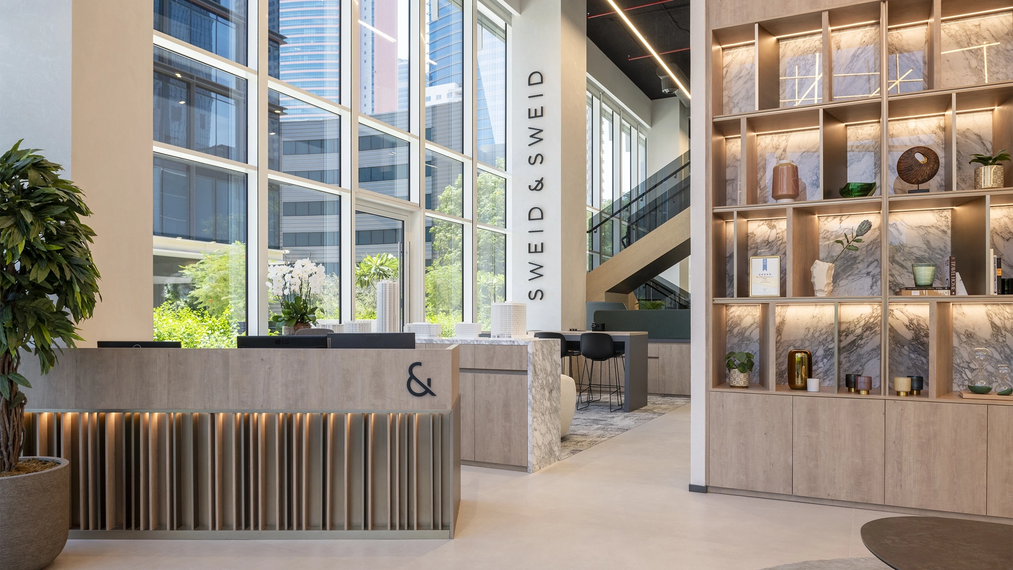 Interior of a warm, light-filled modern office with a shelf of objects and an orchid on the reception desk