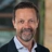 Mark McDonald, Project Director, Infrastructure, outside in front of a blurred brown background featuring a building and mix of natural and urban elements.