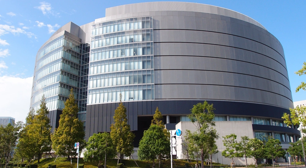 Large grey circular shaped building surrounded by green trees