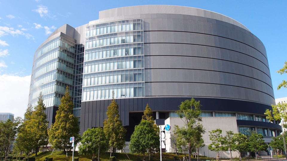 Large grey circular shaped building surrounded by green trees